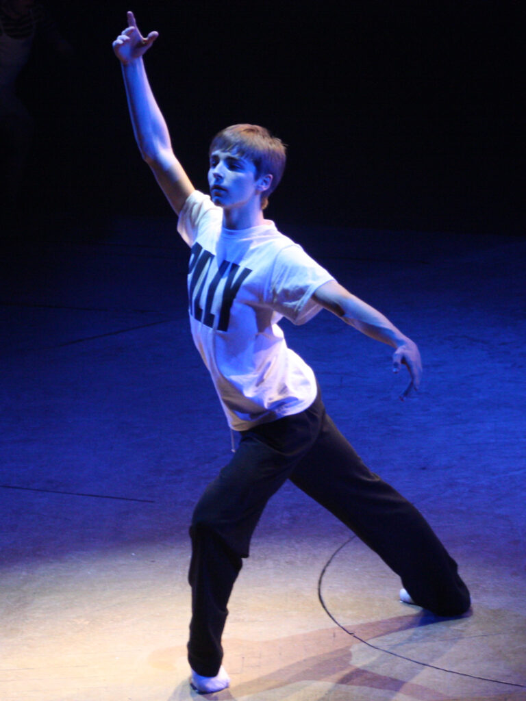 Liam Mower, one of the original actors who played Billy in Billy Elliot the Musical, poses at the show’s fifth anniversary celebration in 2010. He stands smiling in front of a backdrop featuring the musical’s logo