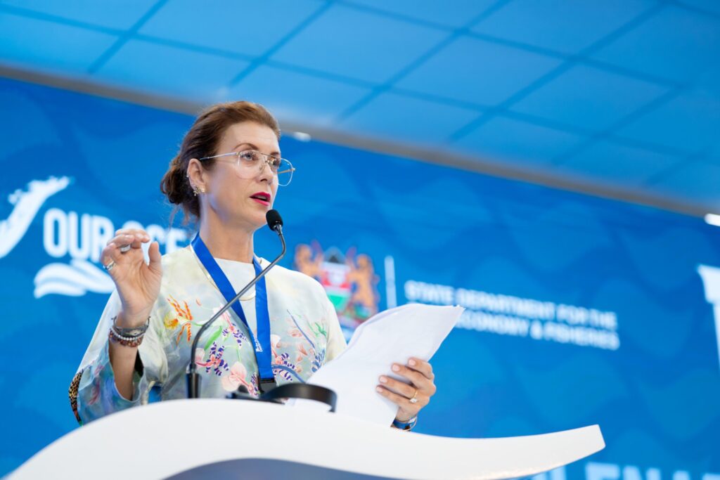 Oceana ambassador Kate Walsh stands at a podium delivering a keynote speech at the Our Ocean Conference in Kenya, holding papers and speaking into a microphone in front of a blue event banner.